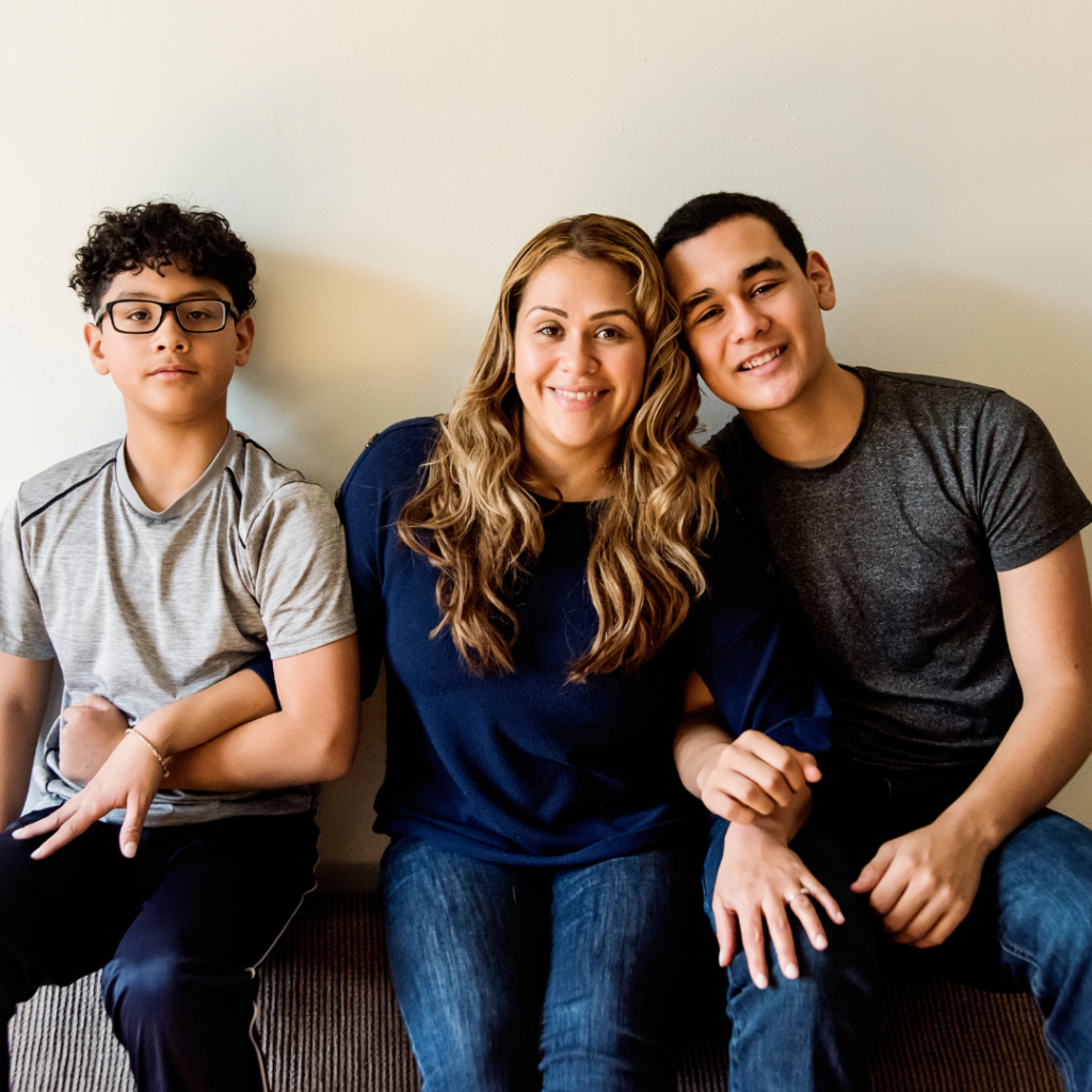 Image of a mother and her two sons. They are sitting next to each other and they look happy.